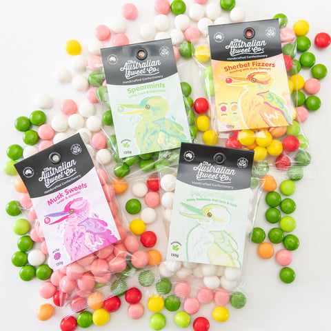 Four packages of Australian Sweet Co candies surrounded by colorful candies on a white background