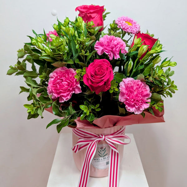 Arrangement of pink flowers with green leaves in a pink container on a white surface.