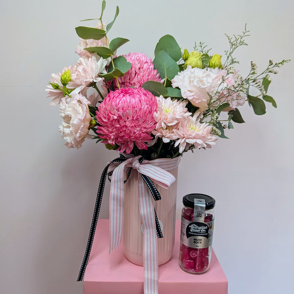 Bouquet of pink and white flowers in a vase on a pink platform with a jar of pink candies.