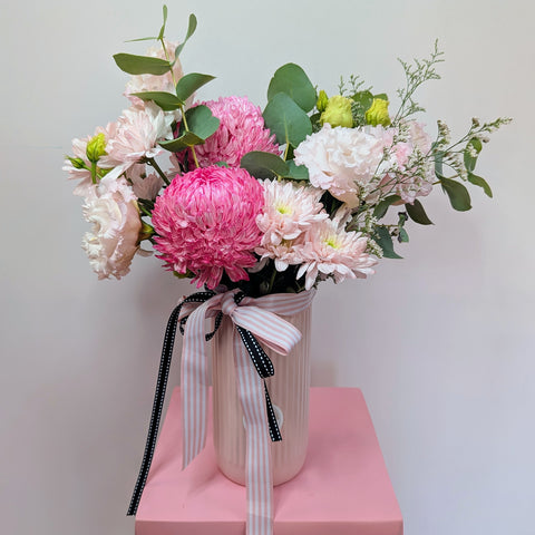 Bouquet of pink and white flowers in a vase with a ribbon on a pink platform against a light gray background