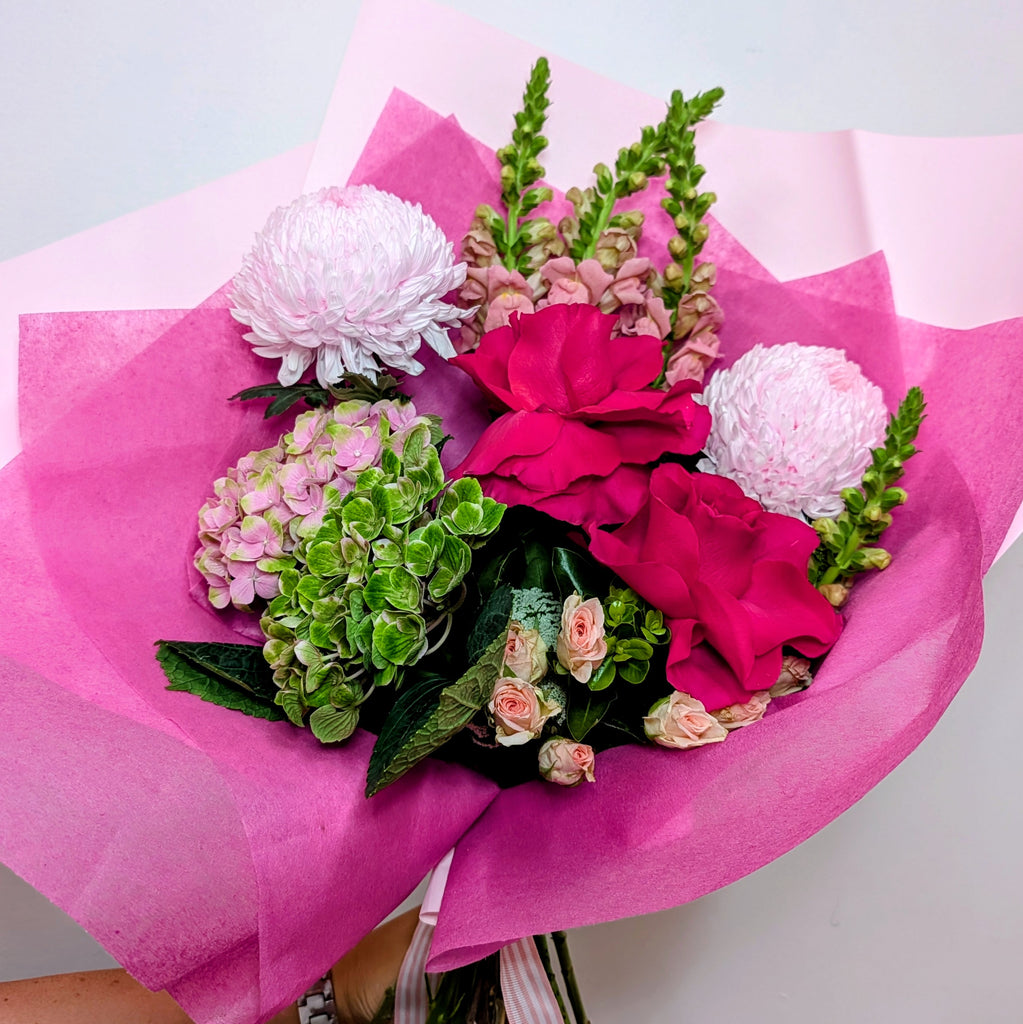 Bouquet of flowers wrapped in pink paper on a light gray background