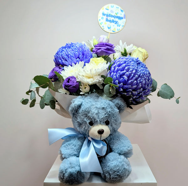 Blue teddy bear with a bouquet of flowers on a white surface