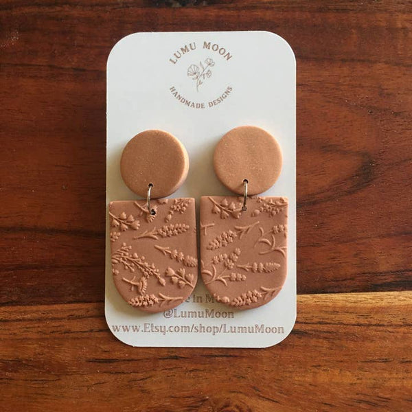 Pair of pink earrings on a LUMU MOON branded card against a wooden background