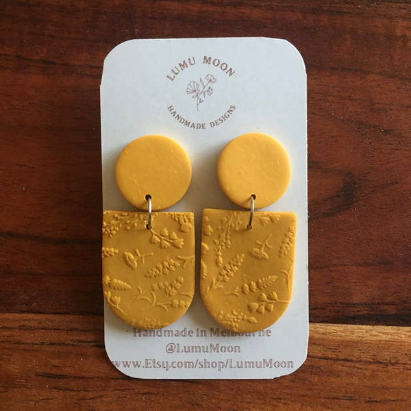 Yellow earrings on a LUMU MOON branded card against a wooden background