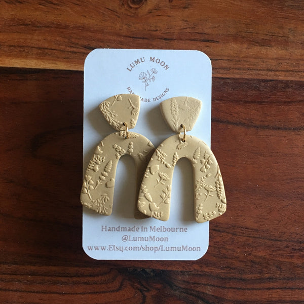 Beige earrings on a LUMU MOON branded card against a wooden background
