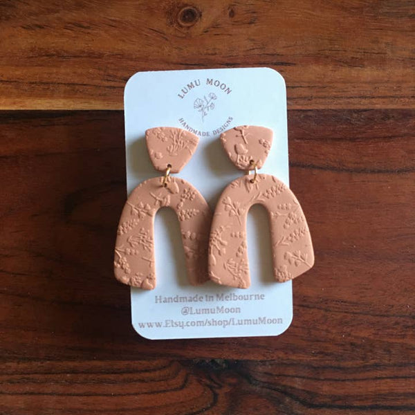 Pair of brown terracotta textured earrings on a Låmu Moøn branded card against a wooden background