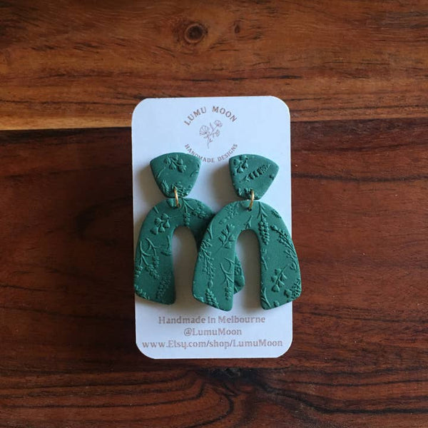 Green earrings on a LUMI MOON branded card against a wooden background