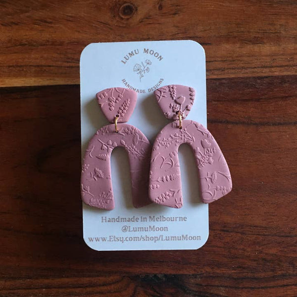 Pink earrings on a LUMU MOON branded card against a wooden background