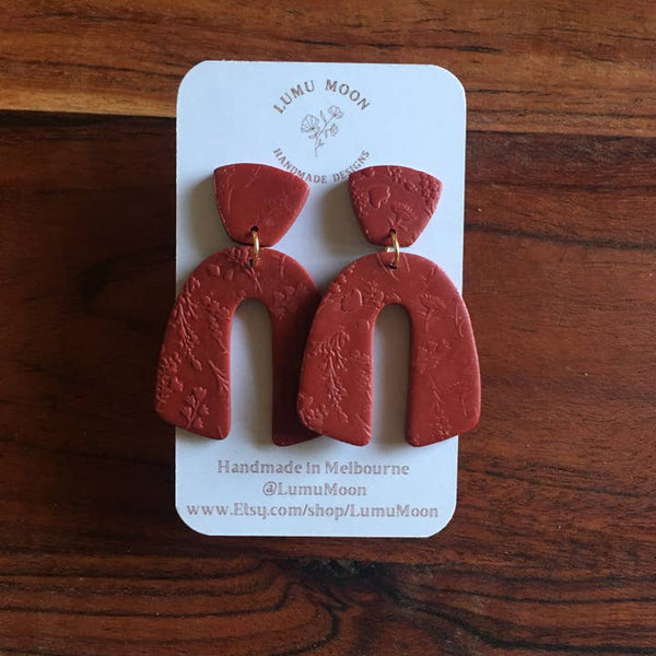 Red earrings on a white card with 'Lumu Moon' branding, displayed on a wooden surface.