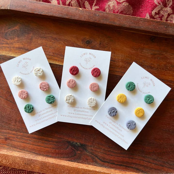 Three cards with colorful earrings on a wooden surface