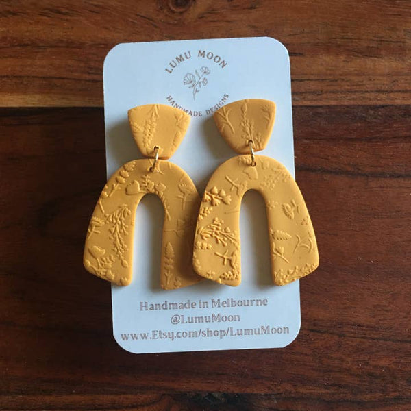 Yellow earrings on a LUMU MOON branded card against a wooden background