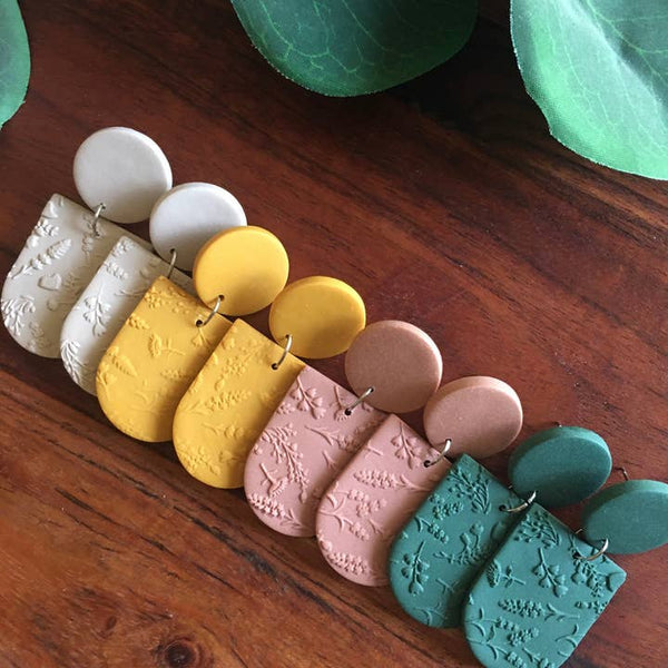 Colorful clay earrings on a wooden surface with green leaves in the background