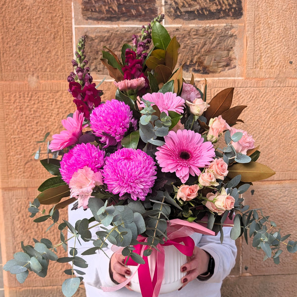 Arrangementof pink and purple flowers with greenery against a stone wall background