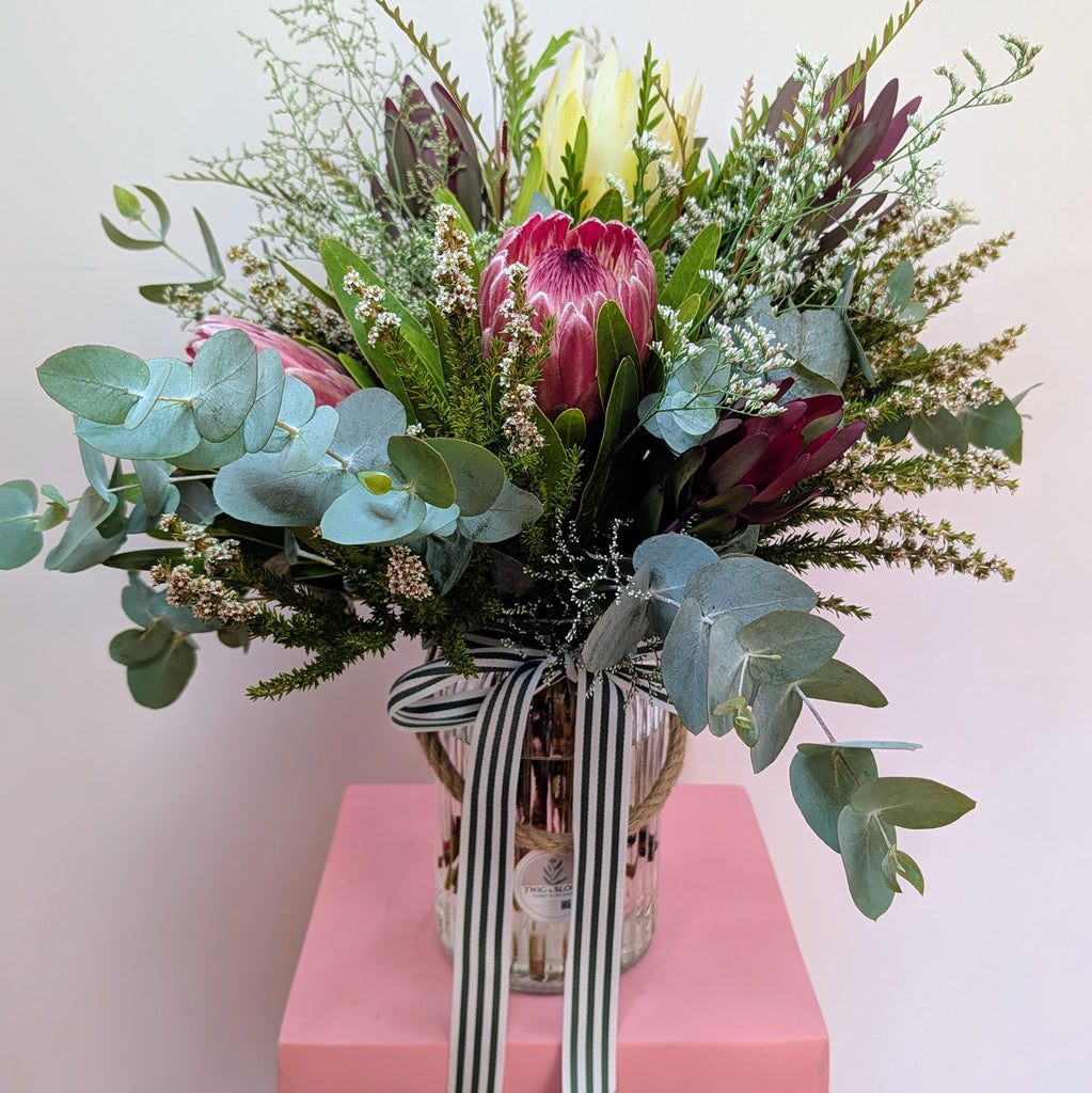 Bouquet of flowers with a striped ribbon in a clear vase on a pink surface.