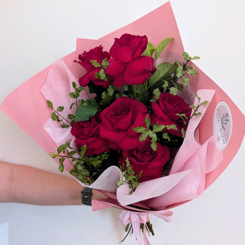 Bouquet of red roses wrapped in pink paper with a white background