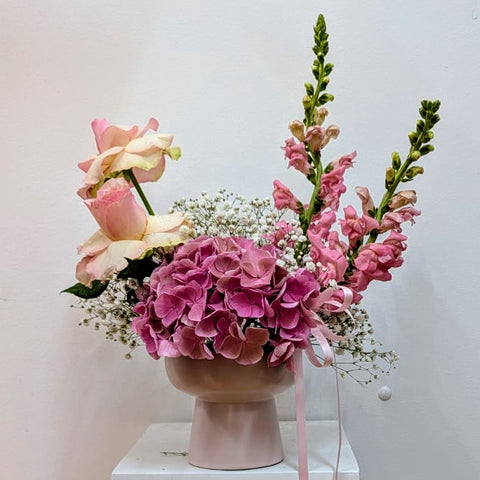 Floral arrangement with pink flowers in a vase on a white surface