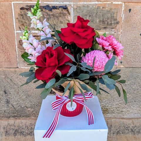 Bouquet of red and pink flowers with a decorative bow on a white box against a stone wall.